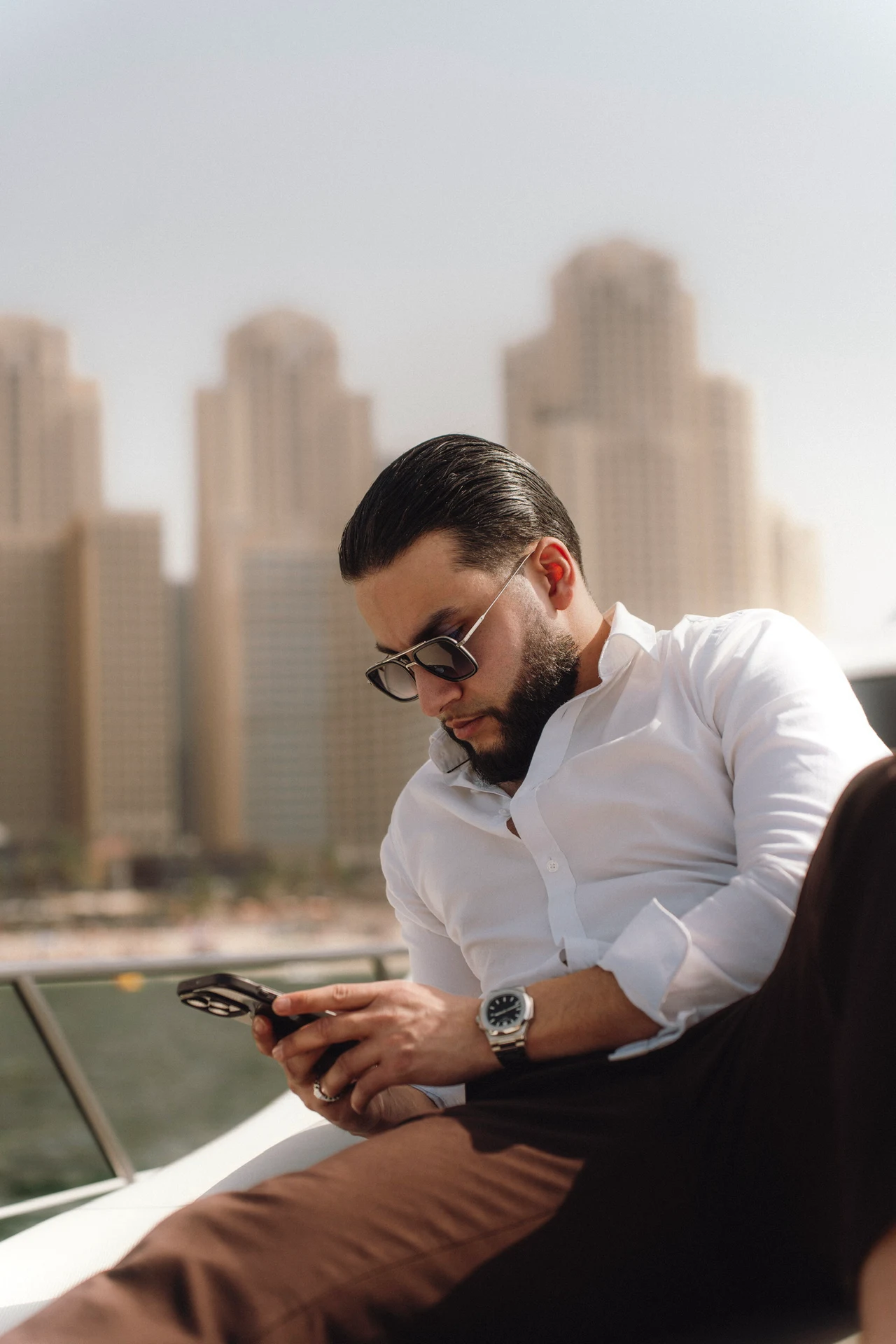 Zack Lalouti in a white shirt and sunglasses looking at his phone aboard a boat in Dubai.