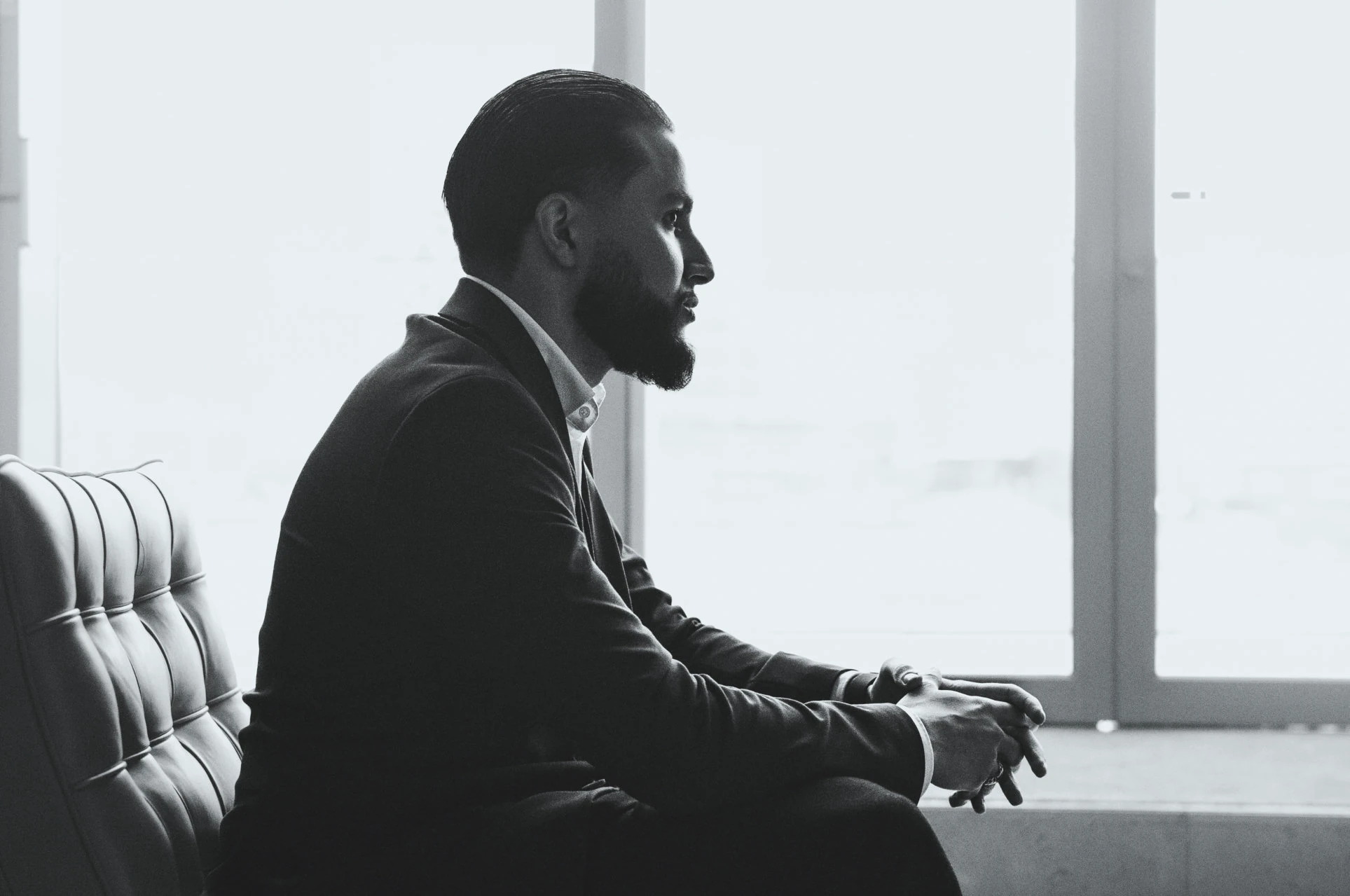 Black-and-white portrait of Zack Lalouti seated in a suit beside a window.