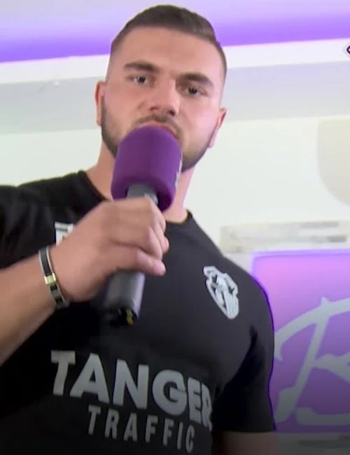 Kosso wearing a black T-shirt and holding a purple microphone during an interview.