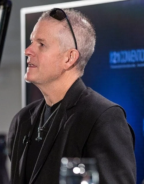 Rollo Tomassi wearing a black jacket and speaking at an event.