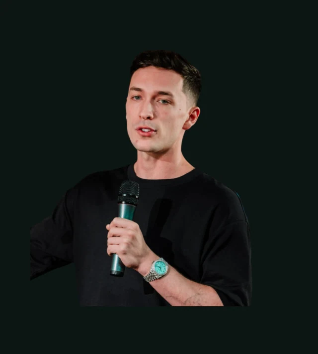 Luke Belmar wearing a black T-shirt and holding a microphone.