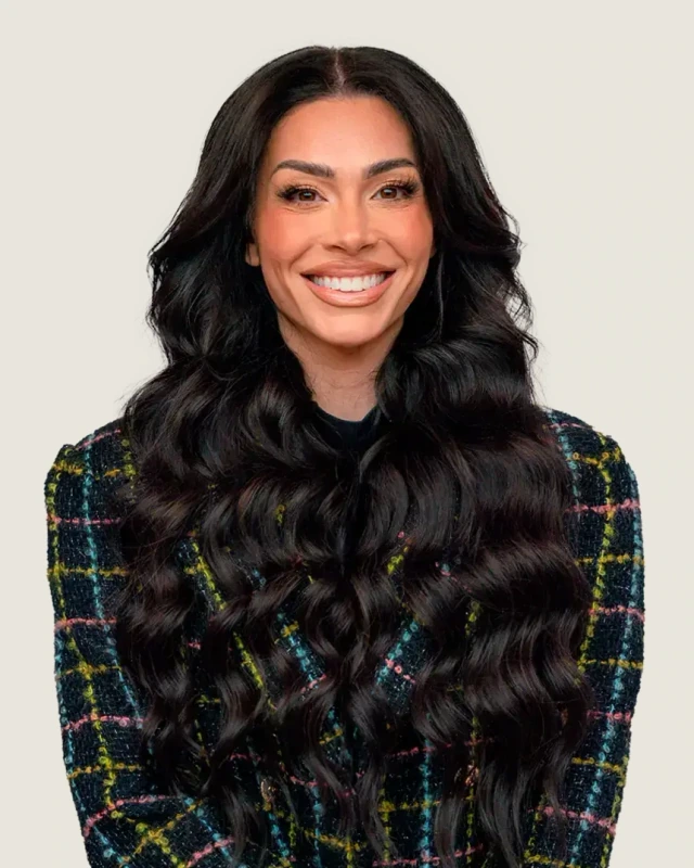 Professional portrait of Leila Hormozi smiling in a dark tweed blazer.